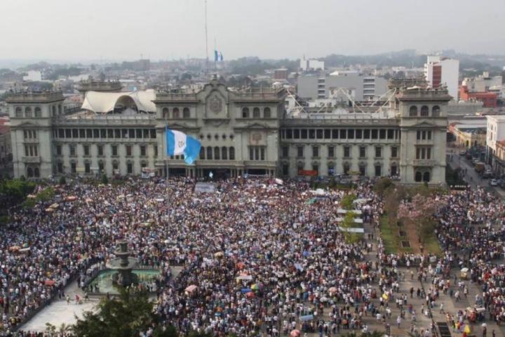 A crowd outside the Palace building in Guatemala City with the Guatemalan flag flying at center.